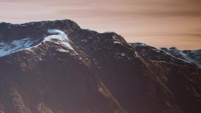 Mountains stand tall with snow on their peaks during sunset. The sky shows colors as the day ends. The scene captures a natural view without people or buildings.