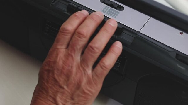 Elderly hand inserting a cassette into a retro stereo, operating a boombox and pressing play
