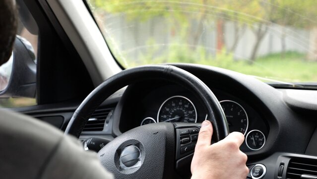 Male arms holds steering wheel while driving a motor car at city. Young man riding on electric automobile at urban road. Driver moving on his electrical auto on route. Slow motion