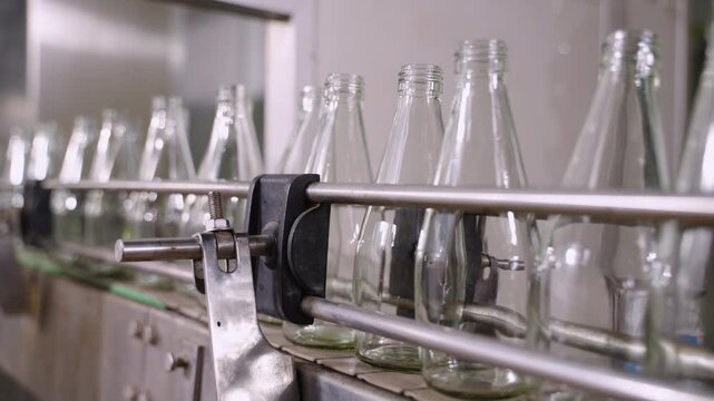 Empty glass beverage bottles on an automatic conveyor belt in a manufacturing plant. Technology for manufacturing bottles and filling fruit juice. Drinking water bottle on factory production conveyor.