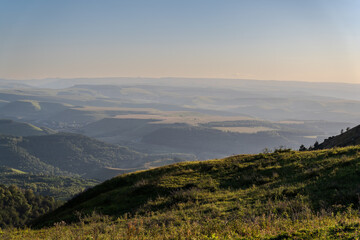 Fototapeta premium Layers of green mountains and hills in the haze during sunset. Panoramic View of Green hills and Meadow.