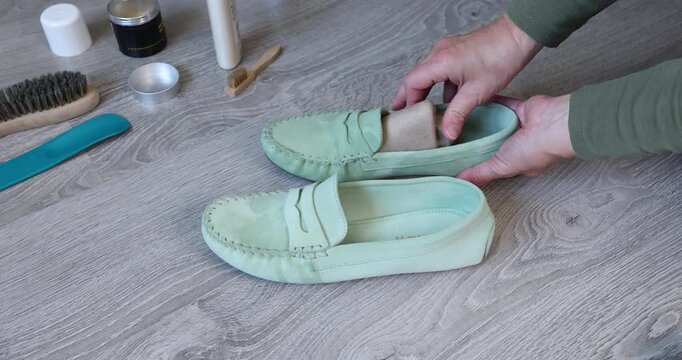 Woman hands inserting cardboard shoe tree shaper into mint green suede loafer. Female person preparing casual nubuck moccasins for seasonal storage or shape preservation during household routine