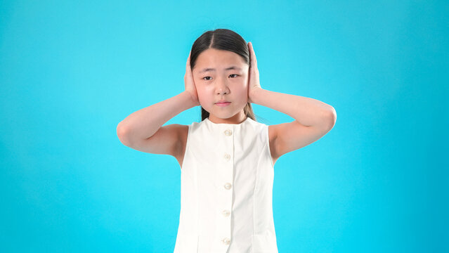 Little girl covering her ears with hands on blue background
