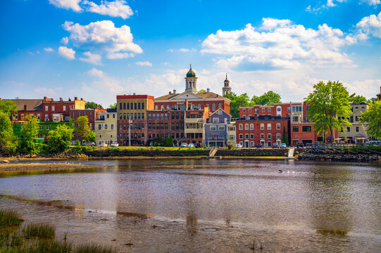 Historic brick buildings and church steeples in Exeter, New Hampshire, viewed across the Squamscott River on a clear summer day.