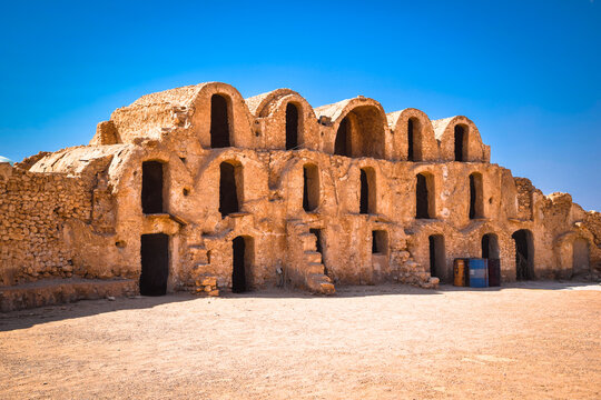 Scenic view of traditional three story clay ghorfas at Ksar Metameur fortified granary under a deep blue sky, Medenine, Tunisia.