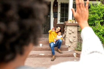 Obraz premium Person waves goodbye to woman with baby on porch steps.
