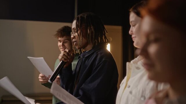 Medium shot of multiethnic teenagers rehearsing performance on stage with African American teenage boy speaking into microphone. Clip for promoting school theater programs and youth arts education