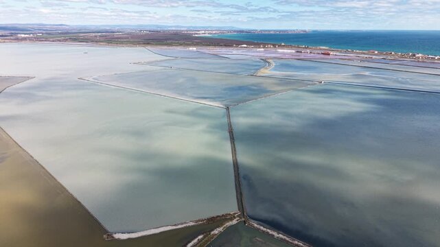 Aerial view of Lake Atanasovsko salt pans with geometric evaporation ponds and narrow paths under a bright sky near the Black Sea coast in Burgas, Bulgaria.