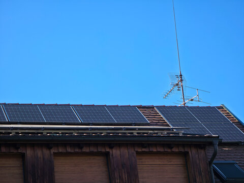 sustainable energy transformation with many pv modules on old house roof and large antenna beneath deep blue sky