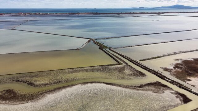 Aerial view of Lake Atanasovsko salt pans with colorful water pools and narrow dikes under a cloudy sky in Burgas, Bulgaria.