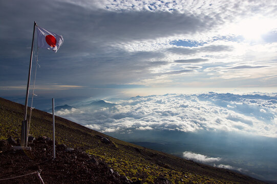 Japanese Hinode flag waving on the mountainside of Mount Fuji with coulds above and below.