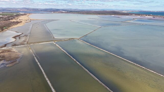 Aerial view of the geometric salt pans and evaporation ponds of Lake Atanasovsko under a blue sky near the coast in Burgas, Bulgaria.