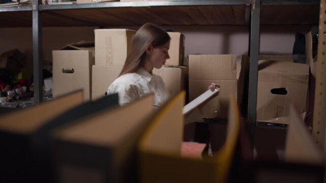 Woman organizing cardboard boxes on metal shelves in a dim storage room