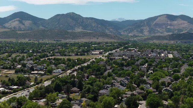Aerial of suburban neighborhood in mountain valley in Jefferson County Colorado with dense single family homes surrounded by mature trees and prominent foothills