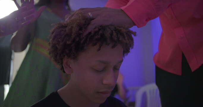 Close up of young boy in prayer with eyes closed as man places hand on his head during solemn church blessing ritual