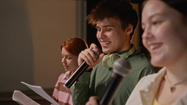 Close up panning shot of diverse teenagers standing on stage in line, holding microphones and rehearsing song together. For high school arts education, theater programs, and student diversity concepts