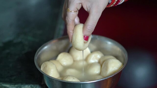 Indian Woman Dipping Soft Rasgulla Sweet into Sugar Syrup Bowl Close Up. Traditional Indian Dessert Preparation with Homemade Rasgulla Sweets.