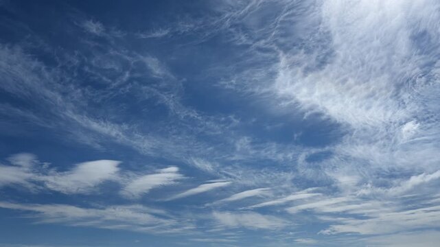 Peaceful time lapse of white summer circus clouds moving across a bright blue sky. Only the clouds are shown
