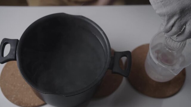 Top view of gloved hands creating thermal shock by alternating hot glass bottle between boiling and iced water, expertly cutting the glass to upcycle it into new object, close-up, slow motion.