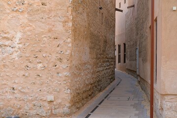 Obraz premium Narrow pedestrian street lined with traditional buildings in UAE. Historic architecture, textured walls and heritage urban environment.