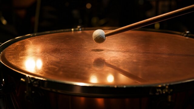Close-up of a timpani drumhead with a drumstick poised just above its center.