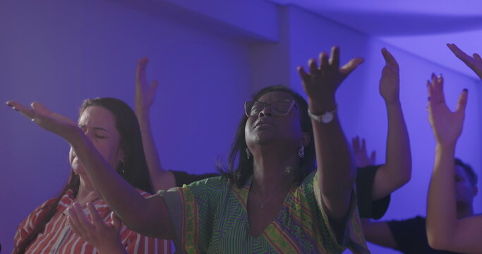 Diverse congregation praying with eyes closed and hands raised during evangelical church service, expressing spiritual intensity, unity, and shared devotion