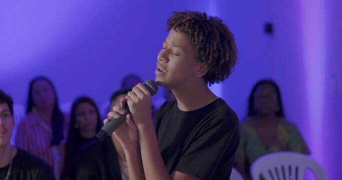 Young African American teenager singing passionately with microphone during Christian evangelical worship service, congregation in background