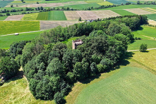 Historischer R&ouml;merturm inmitten eines dichten, gr&uuml;nen Waldst&uuml;cks, umgeben von weiten Feldern und Wiesen in einer idyllischen l&auml;ndlichen Landschaft aus der Vogelperspektive fotografiert.