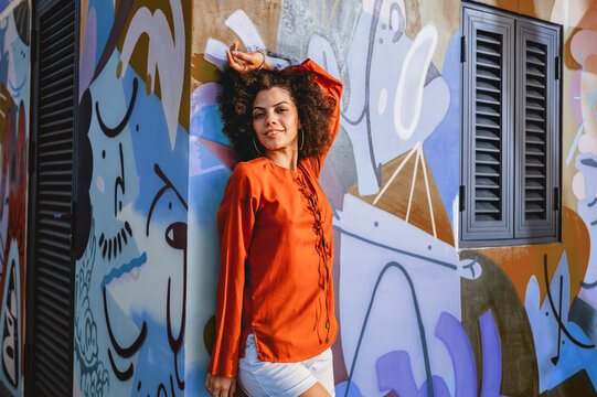 Woman radiates pure love of life, smiling against a vibrant, expressive urban backdrop