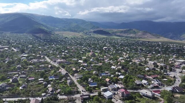 Beautiful aerial drone shot of the scenic Odzun village in Armenia, showing charming houses surrounded by lush green trees and majestic mountains under a bright summer blue sky.

