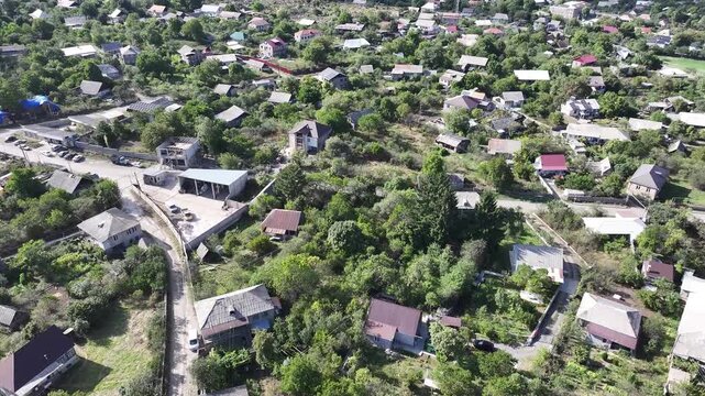 Beautiful aerial drone shot of the scenic Odzun village in Armenia, showing charming houses surrounded by lush green trees and majestic mountains under a bright summer blue sky.

