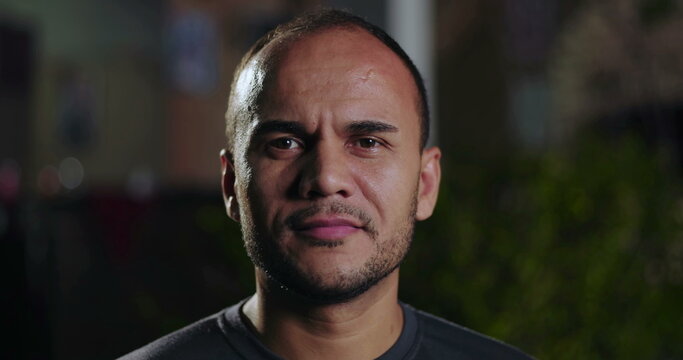 Closeup portrait of Latin Hispanic man with serious expression standing outdoors at night with soft background blur and focused facial features