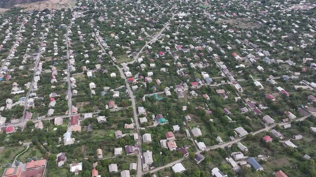 Beautiful aerial drone shot of the scenic Odzun village in Armenia, showing charming houses surrounded by lush green trees and majestic mountains under a bright summer blue sky.

