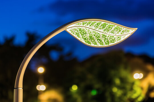 Futuristic eco-friendly street lamp shaped like a glowing green leaf at night