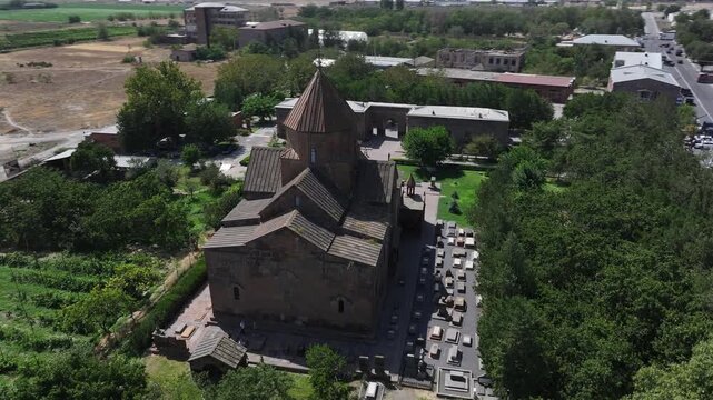 An aerial drone shot captures the historic Saint Gayane Church, an ancient Armenian apostolic church showcasing its beautiful stone architecture and green courtyard in the city of Vagharshapat.

