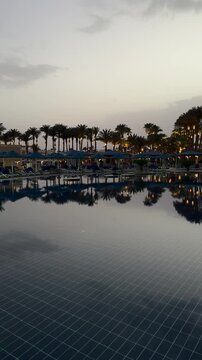 Twilight at a resort pool. Palm trees reflect in calm water. Very soft gentle lights and long dark shadows create a beautiful peaceful warm tropical serene atmosphere!!