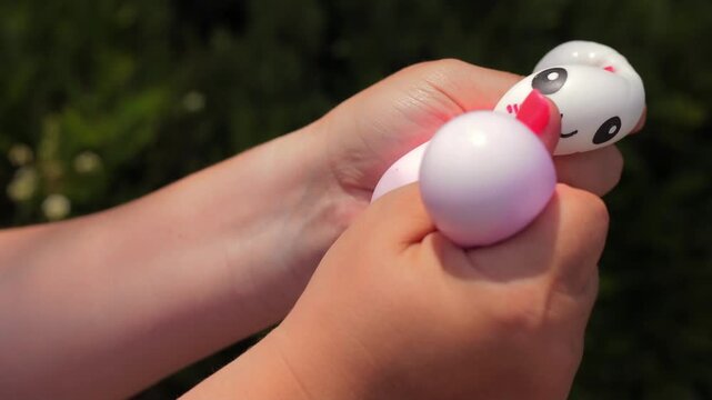 Two hands holding stack of three kawaii squishy dumpling toys in white, pink and lavender with cute faces outdoors