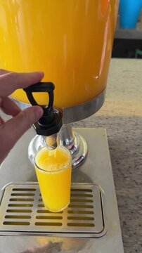 Pouring orange juice from a dispenser, close point-of-view, fresh stream into glass, bright breakfast moment.