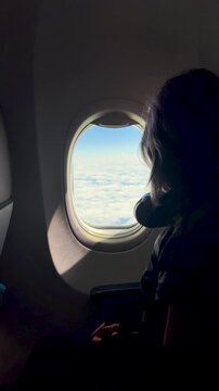 Girl airplane passenger gazes out window at clouds and sky, peaceful flight, travel wonder, childhood curiosity.