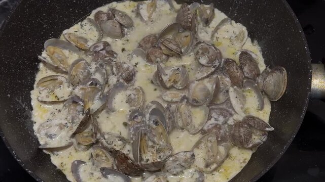 Cooking vongole clams in a wine-cream sauce on a skillet, garlic, parsley, steaming, rich seafood.
