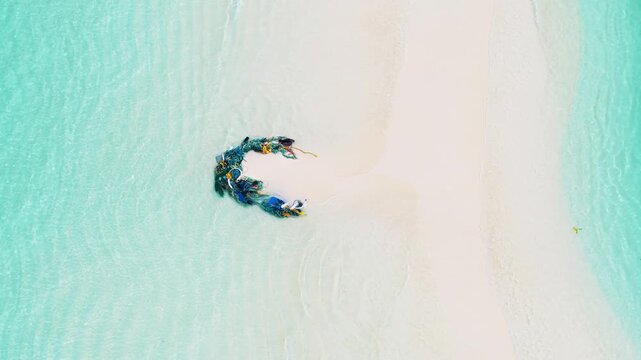 Aerial view of a pile of discarded fishing nets washed up on a pristine white sandbank surrounded by turquoise ocean water in Kudahuvadhoo, Dhaalu Atoll, Maldives.