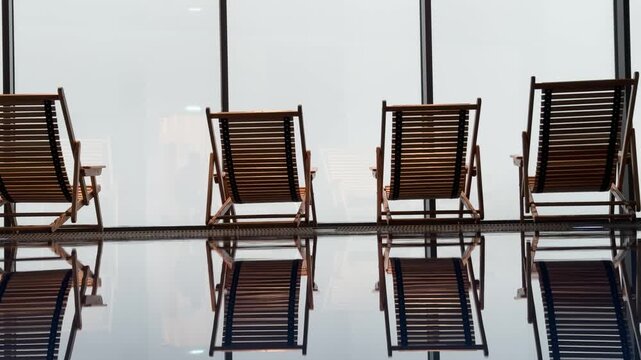 Row of loungers around pool before panoramic window overlooking metropolis, urban luxury meets serene water.
