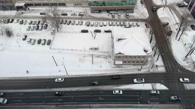 Timelapse from high floor: winter city traffic on snowy roads, red and white light streaks, cold aerial perspective. Urban winter scene, traffic flows slowly. Aerial view high up!