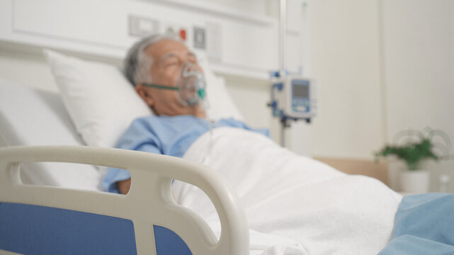 Asian old man lying on hospital bed wearing oxygen mask. Ill patient receiving respiratory therapy in clinics. Critical care medicine and treatment for breathing problem or infection.
