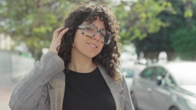 Woman adjusting oversized patterned glasses and touching her hair on a street; confidence ease authenticity.