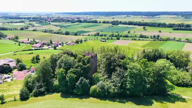 Historischer R&ouml;merturm inmitten eines dichten, gr&uuml;nen Waldst&uuml;cks, umgeben von weiten Feldern und Wiesen in einer idyllischen l&auml;ndlichen Landschaft aus der Vogelperspektive fotografiert.
