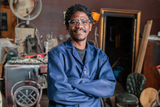 Smiling African worker stands in workshop with tools after successful working day