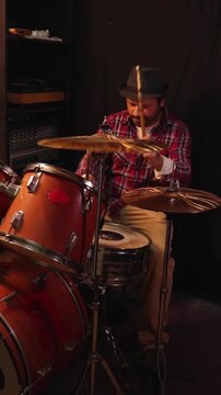 Passionate male musician drumming with drumsticks during an intense studio session, vertical format
