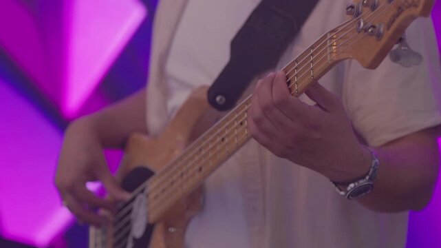 Close-up of bassist hands performing on stage with purple geometric backlighting during concert