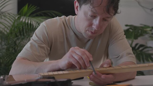 Hands performing progressive guitar nut shaping and setup on headstock during maintenance sequence